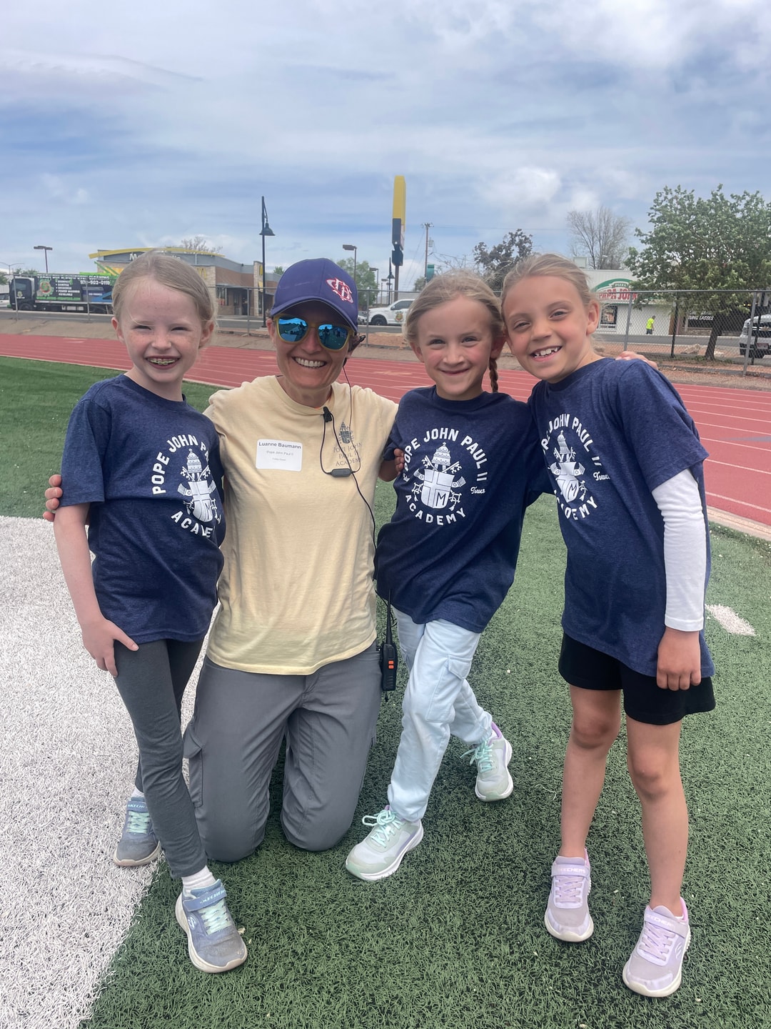 Students and Ms. Baumann celebrating together on the track field at Pope John Paul II Academy